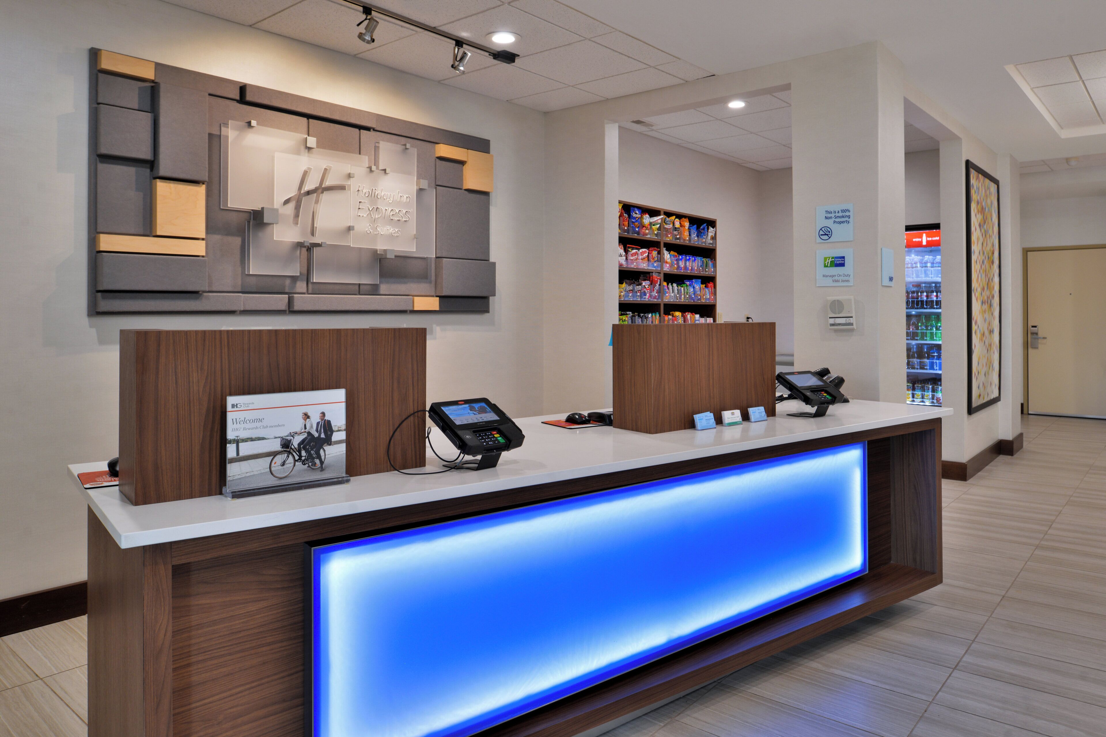 Un comptoir d’accueil d’hôtel avec un éclairage bleu, un kiosque numérique et un écran fixé au mur.