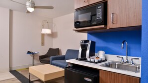 A compact kitchenette with a microwave, coffee maker, and sink. There's a small refrigerator, a sofa, and a table with a lamp. - Holiday Inn Express & Suites Cincinnati - Mason by IHG (Mason)