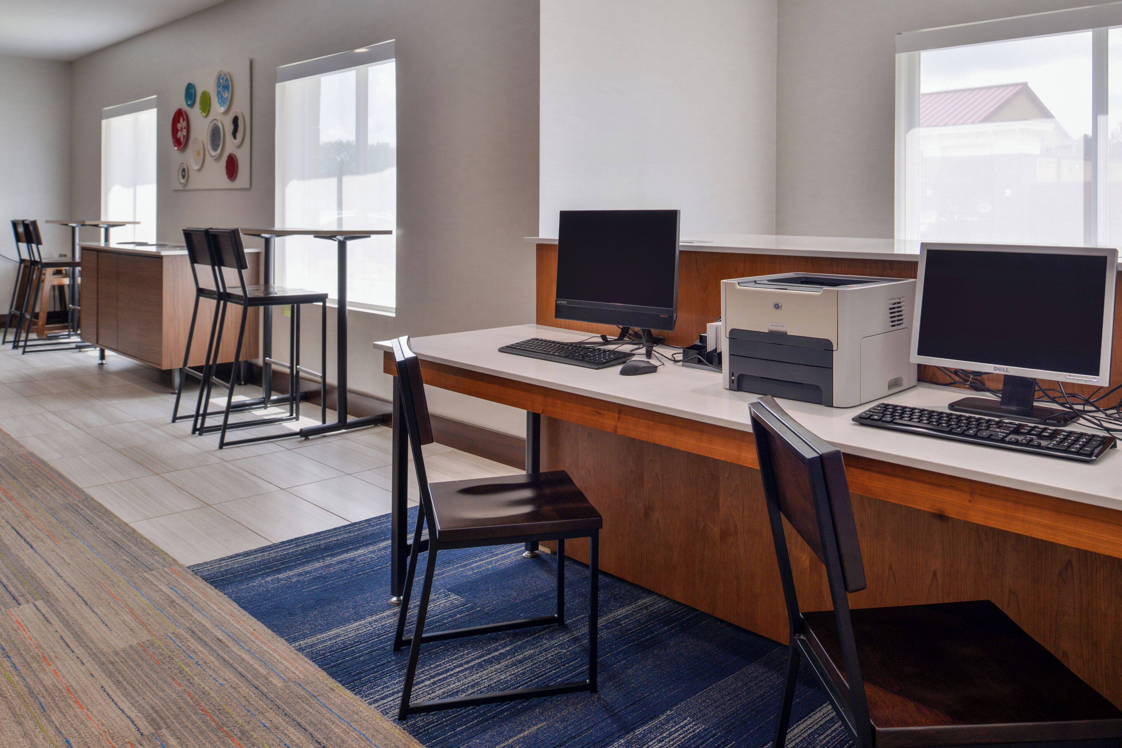 A modern office space with a long desk, two computer monitors, a printer, and a keyboard.