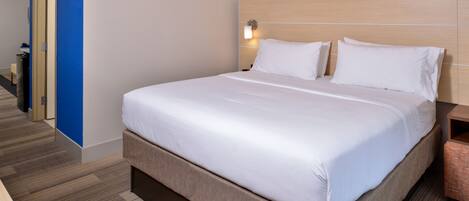 Quarto de hotel com uma cama grande, cabeceira de madeira, mesa de cabeceira e uma parede azul.