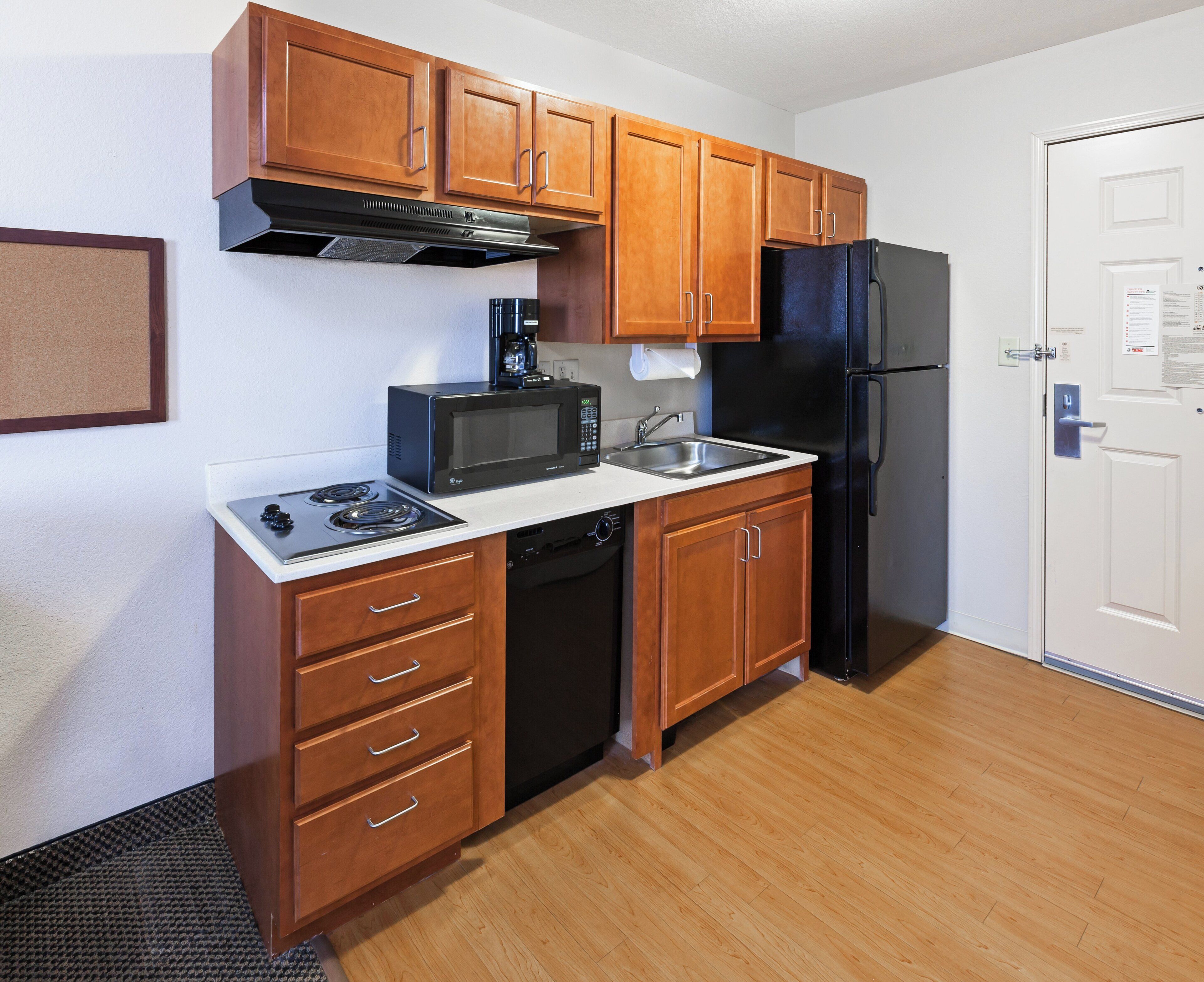 A compact kitchen with wooden cabinets, a black refrigerator, a microwave, a coffee maker, and a dishwasher.