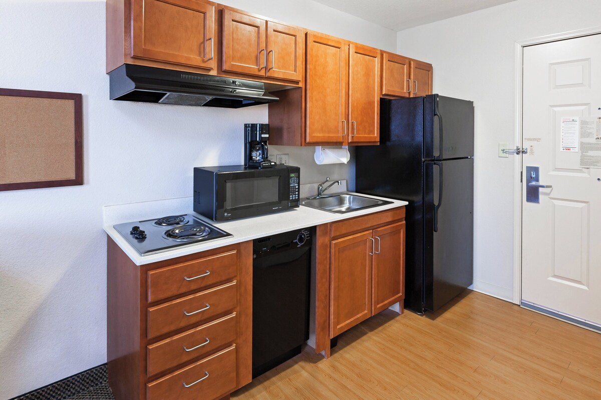 A compact kitchen with wooden cabinets, a black refrigerator, a microwave, a coffee maker, and a dishwasher.