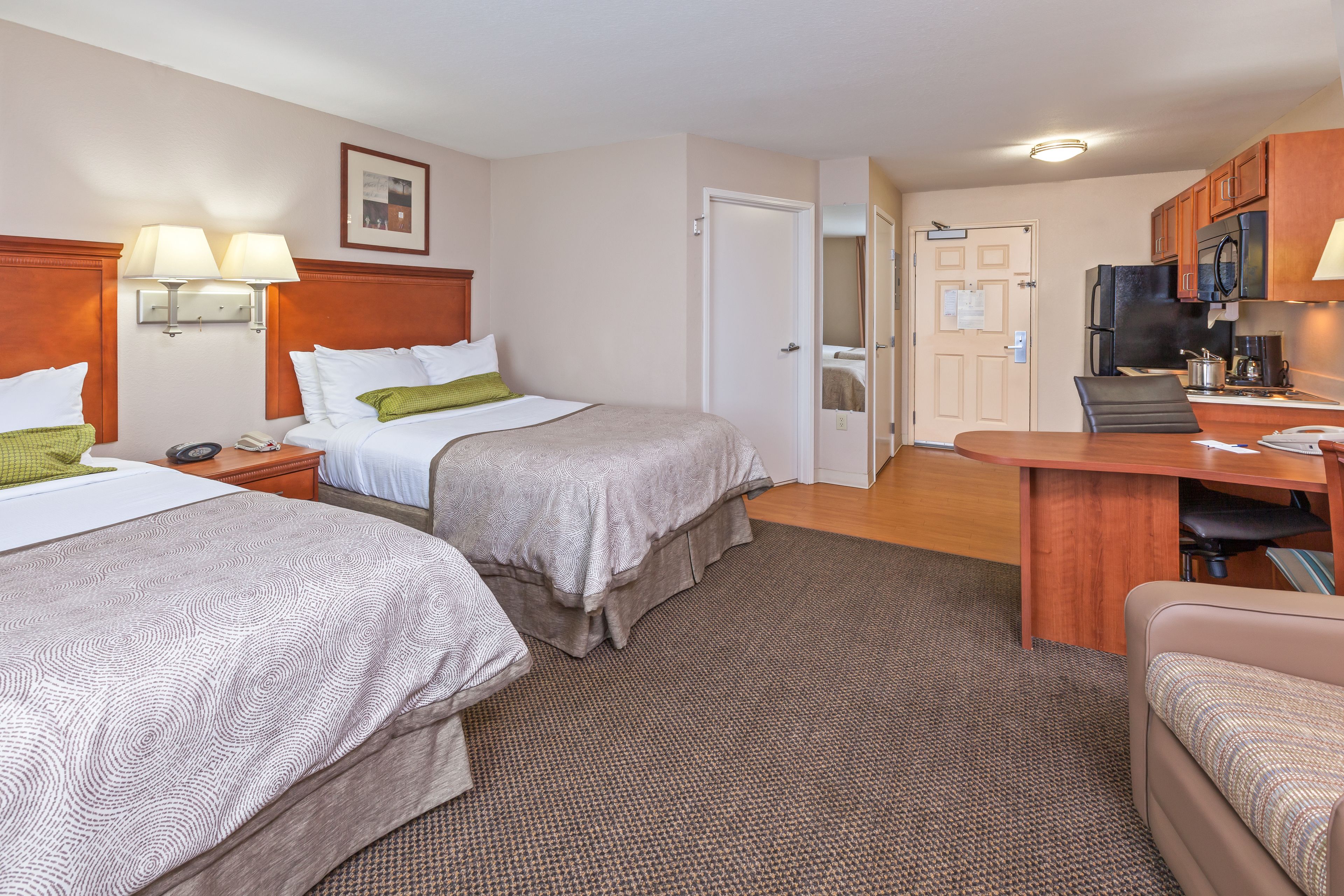 A hotel room with two beds, a desk, a chair, a refrigerator, and a microwave.