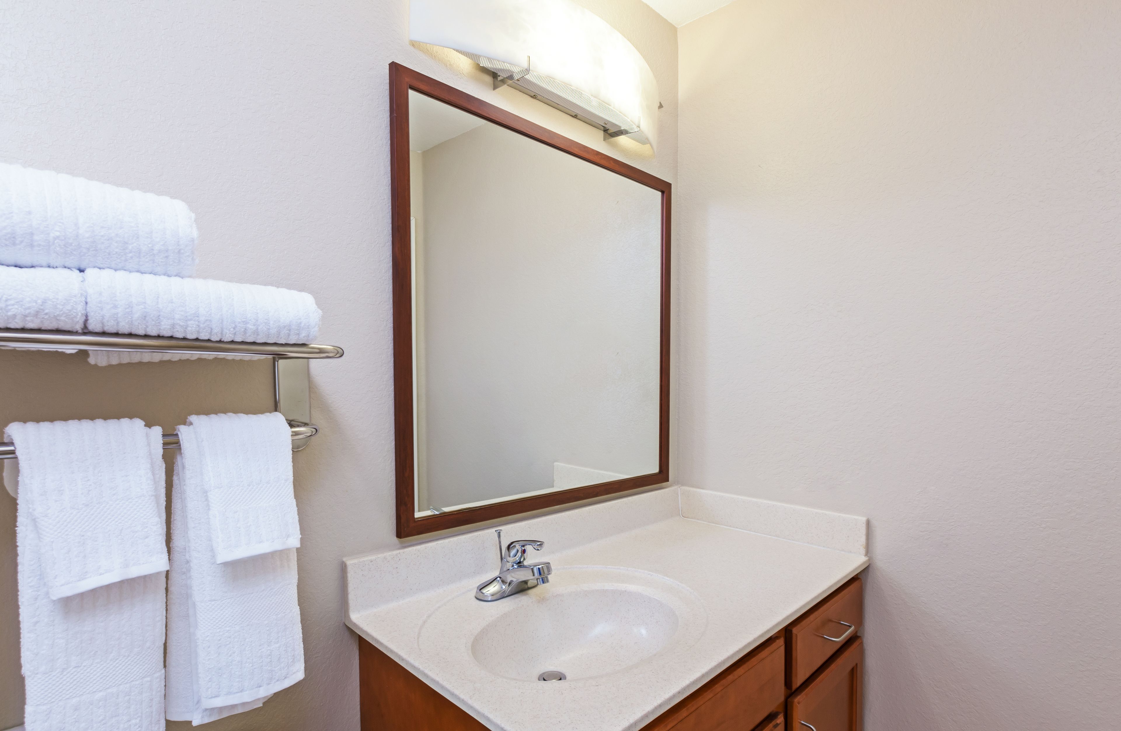 A bathroom with a white sink, a mirror, and a towel rack with folded towels.