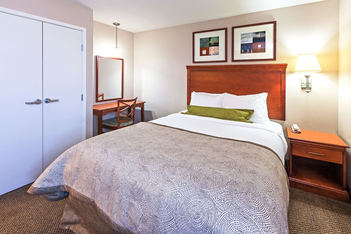 Hotellihuoneessa on suuri sänky, puinen yöpöytä, työpöytä ja tuoli. Sängyn yläpuolella seinällä on kaksi kehystettyä kuvaa.