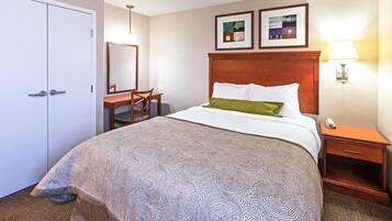 A hotel room with a large bed, a wooden nightstand, a desk, and a chair. There are two framed pictures on the wall above the bed.