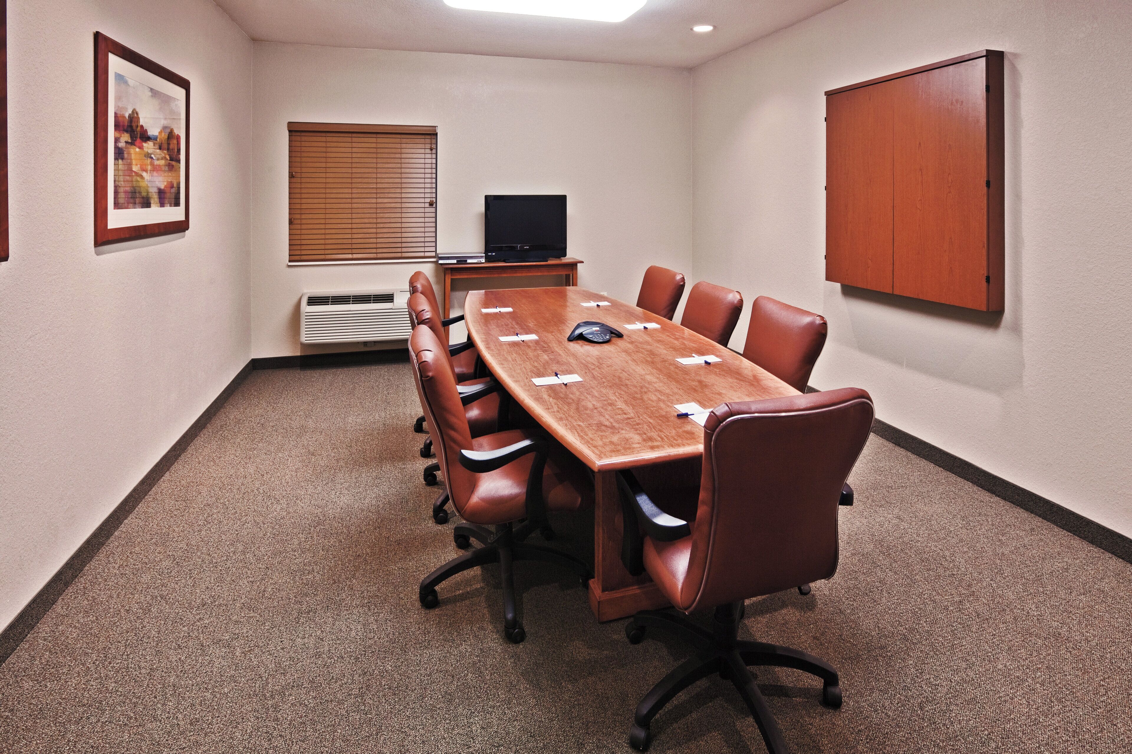 A conference room with a long table, leather chairs, a television, and a cabinet.
