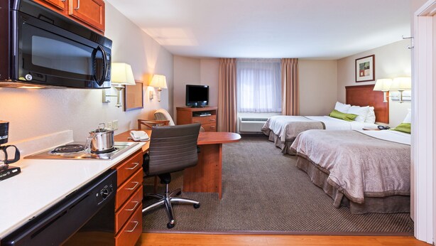 Quarto de hotel com cozinha compacta, uma cama, uma escrivaninha e uma televisão.