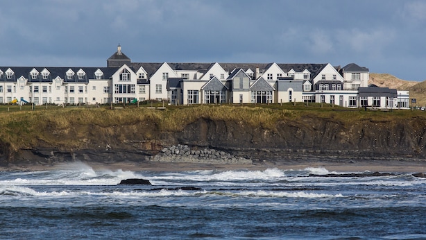 Un hôtel en bord de mer, doté de plusieurs toits à pignons, situé sur une falaise surplombant la mer.