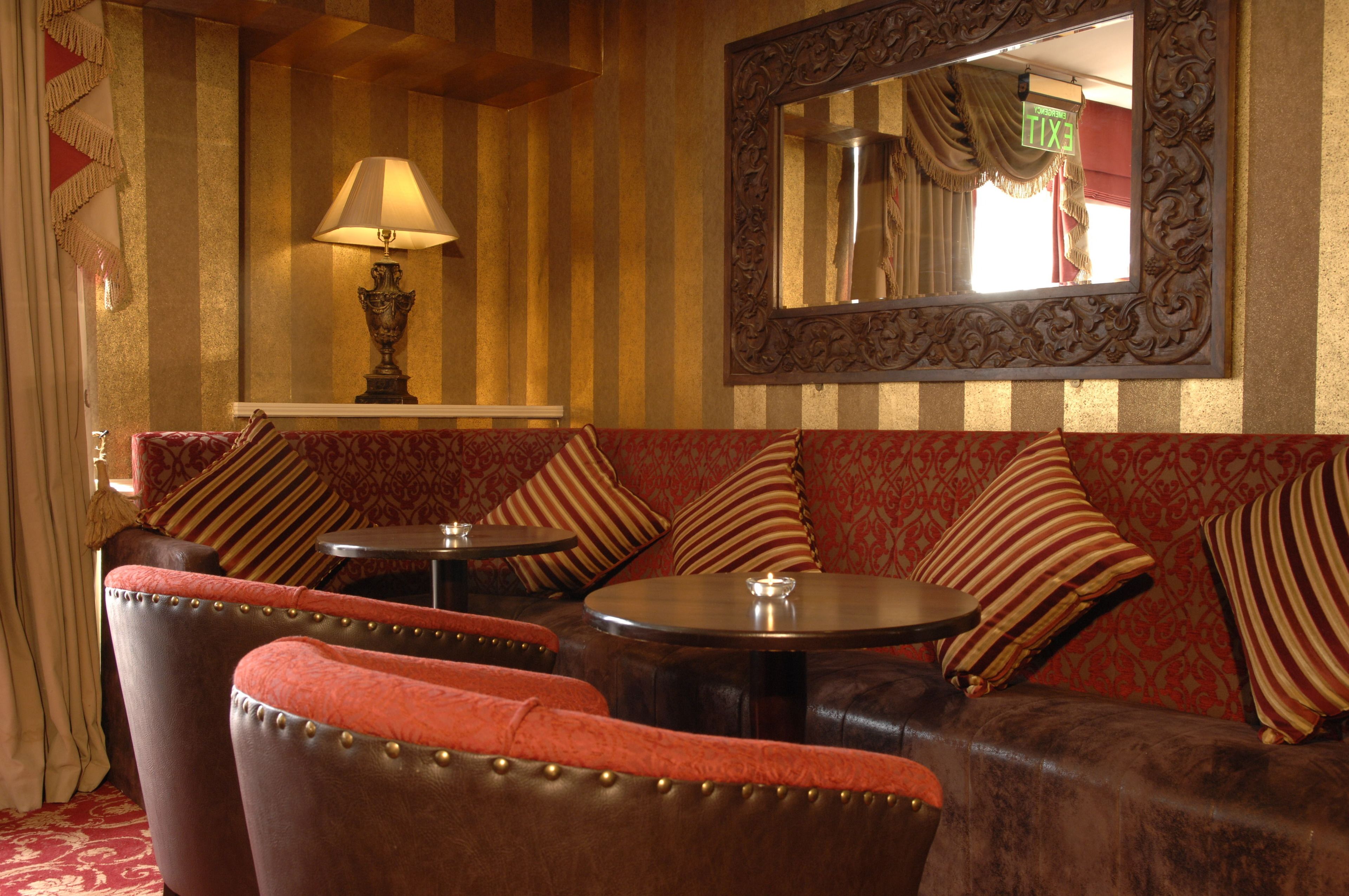 A room with striped wallpaper, a sofa with striped cushions, a table with a lamp, and a mirror on the wall.