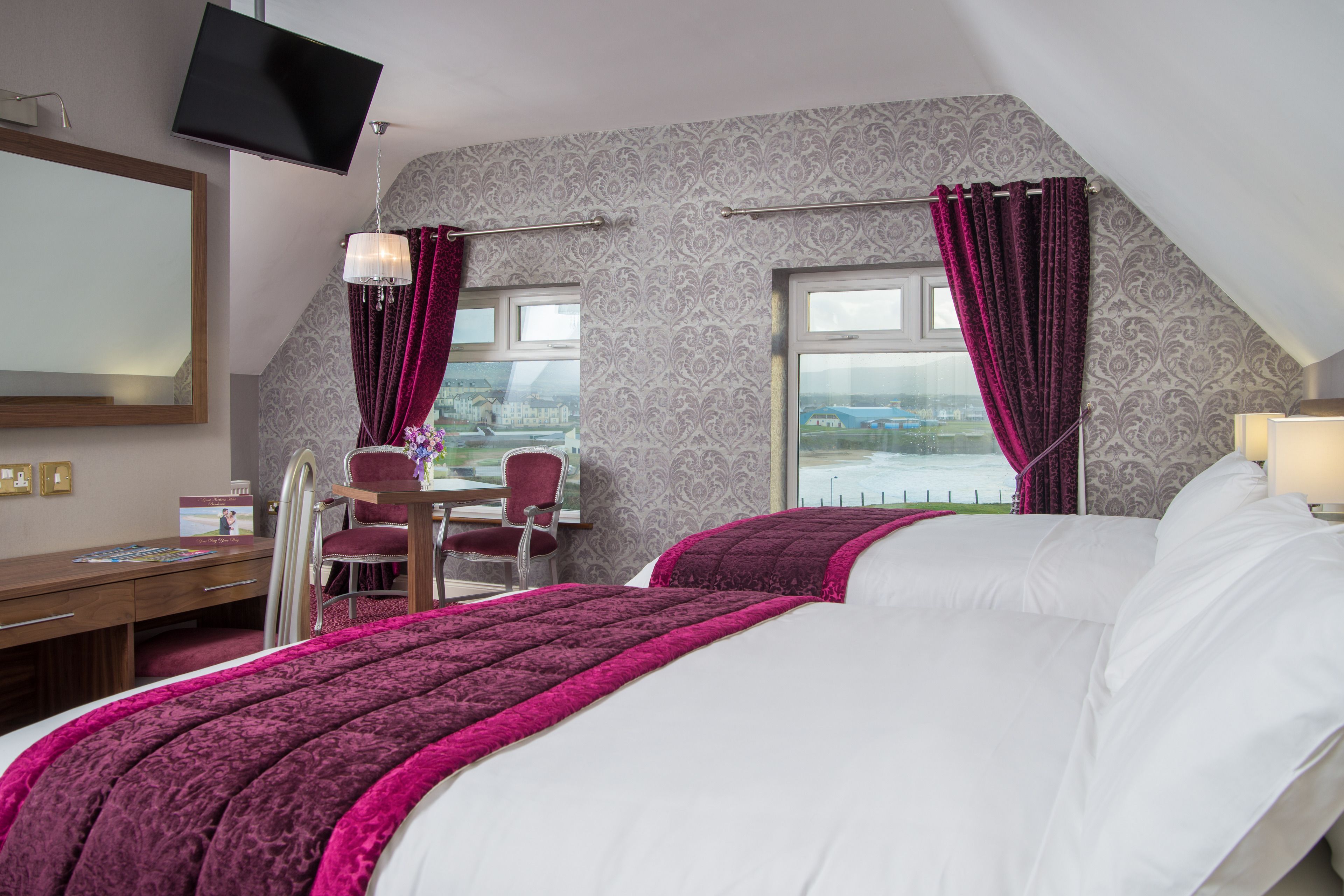 Ein Hotelzimmer mit einem großen Bett, einem Schreibtisch und einem Stuhl. An der Wand ist ein Fernseher befestigt und das Zimmer bietet einen Ausblick nach draußen.