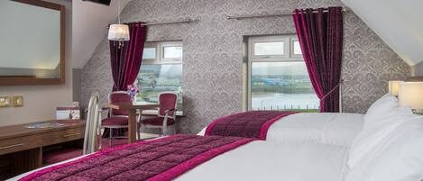 Une chambre d’hôtel avec un grand lit, un bureau et une chaise. Un téléviseur est fixé au mur, et la chambre offre une vue sur l’extérieur.