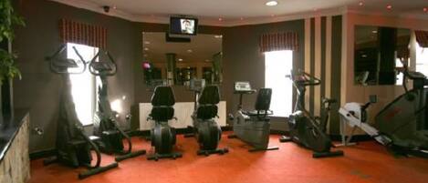 A gym with various exercise machines, a television on the wall, and a red carpeted floor.