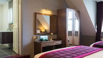 Una habitación de hotel con cama, escritorio con una computadora portátil, armario y baño visible a través de una puerta abierta.