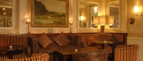 A cozy lounge area with striped upholstered seating, a large painting on the wall, and wall-mounted lamps.