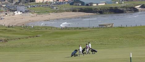 A coastal golf course with a beach and buildings in the background.