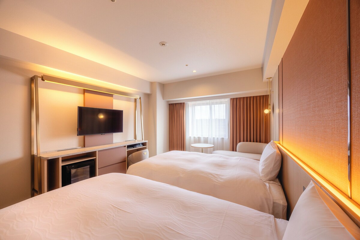 A hotel room with two beds, a TV, a desk, and a small table.