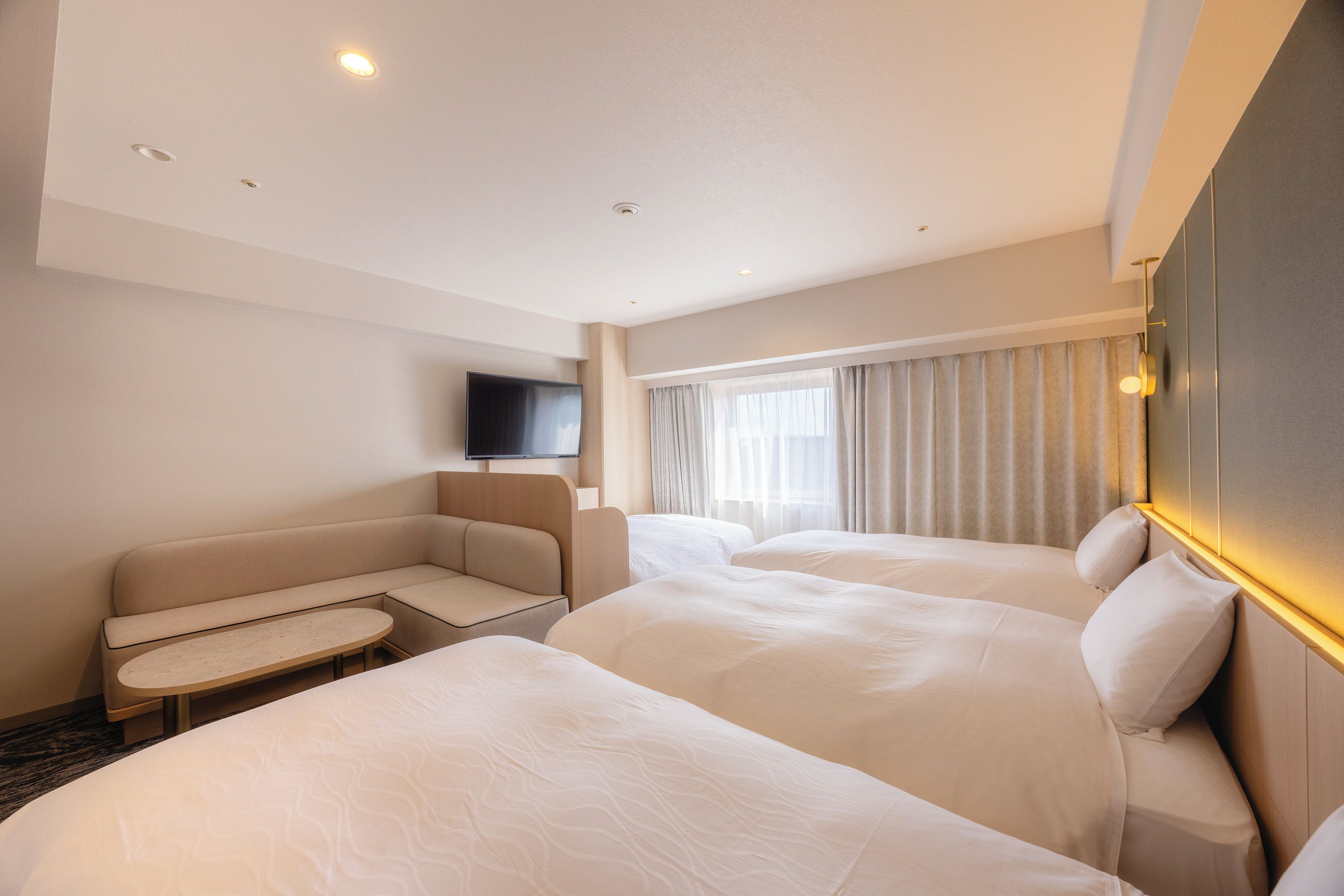 A hotel room with two beds, a sofa, a small table, and a TV.