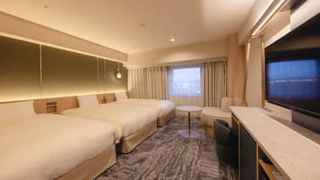 A hotel room with two beds, a small round table, a sofa, a TV, and a window with curtains.
