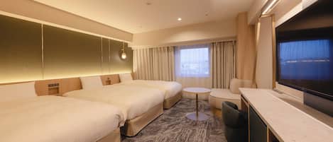 A hotel room with two beds, a small round table, a sofa, a TV, and a window with curtains.