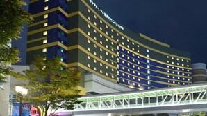 Ein mehrstöckiges Hotel mit einer geschwungenen Fassade, beleuchteten Fenstern und einer Fußgängerbrücke.