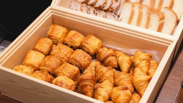 Een houten doos gevuld met gebakjes, waaronder croissants en sneetjes brood.