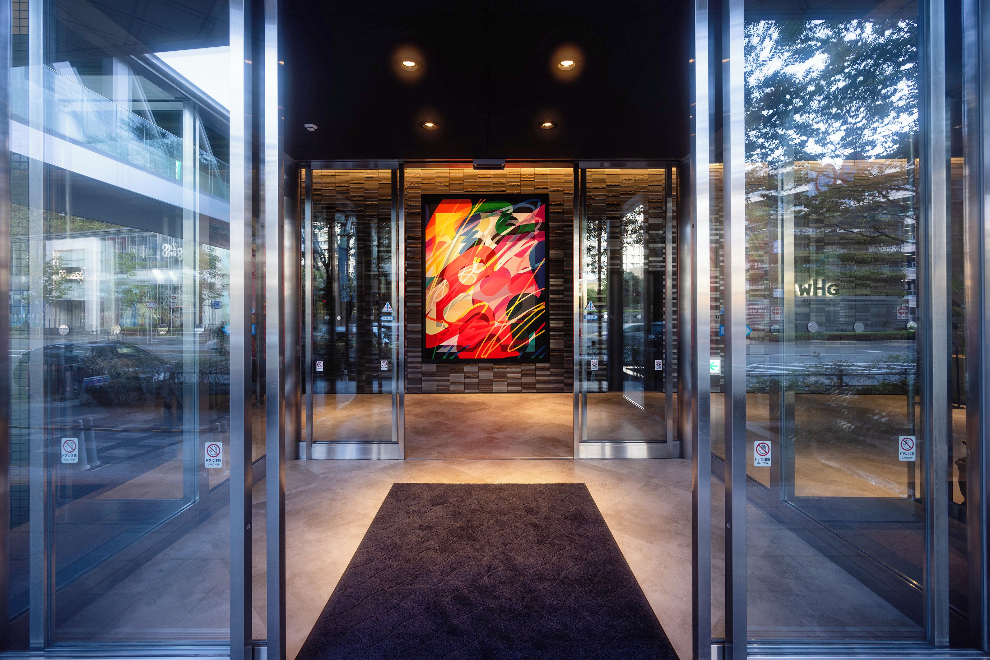 A modern building entrance with glass doors, a central art piece, and a carpeted floor.