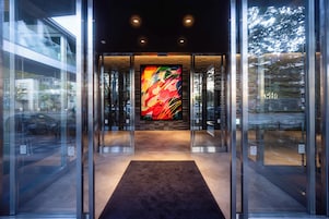 Entrada de un edificio moderno con puertas de vidrio, una pieza de arte central y suelo alfombrado.
