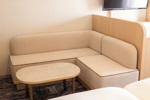 A corner seating area with a sofa and a small table, a television mounted on the wall, and a carpeted floor. - Canal City Fukuoka Washington Hotel (Fukuoka)