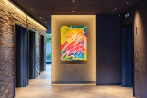 A modern hallway with a colorful abstract painting on the wall, a brick-patterned wall on the left, and a dark-colored elevator on the right. - Canal City Fukuoka Washington Hotel (Fukuoka)