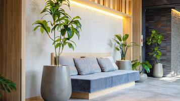 A modern interior with a sofa, large potted plants, and a textured wall.