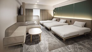 Ein modernes Hotelzimmer mit einer Sitzecke, zwei Einzelbetten, einem kleinen Tisch und einem Fernseher.