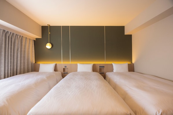 A hotel room with two beds, a bedside table, a lamp, and a curtain.