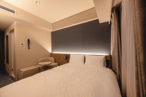 Habitación de hotel con una cama grande, una mesita de noche, una silla, una pequeña mesa y un teléfono en la pared.