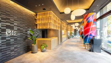 A modern hotel reception area with a reception desk, potted plants, and a colorful wall mural.