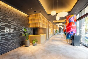 A modern hotel reception area with a reception desk, potted plants, and a colorful wall mural.