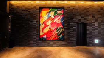 A modern interior with a large abstract painting on a textured wall, a dark elevator, and a polished floor.