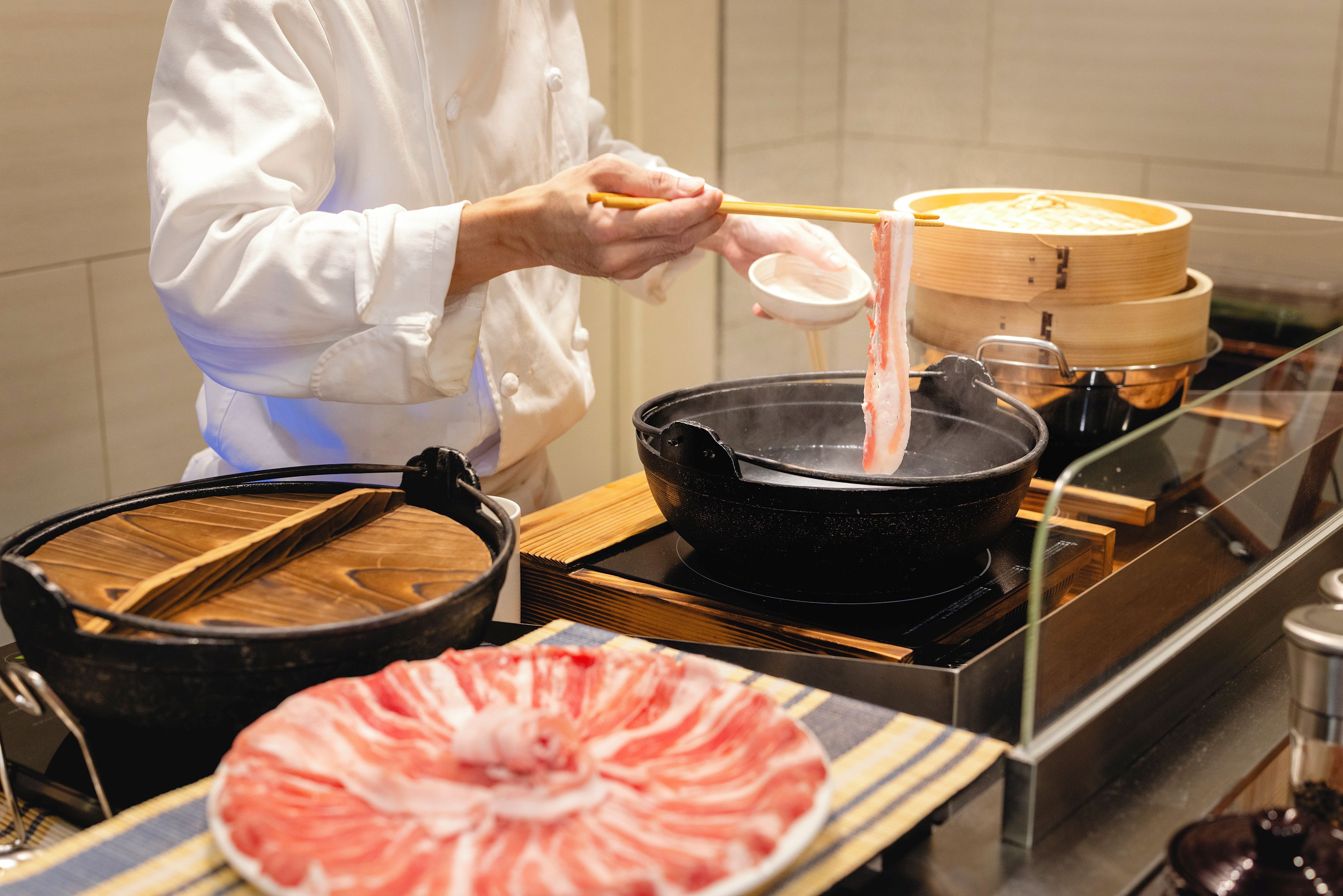 A person in a white coat preparing food with chopsticks over a pot on a stove.