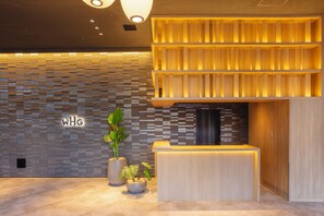Ett välkomnande område med modern design, med en reception i trä, en vägg med ett geometriskt mönster och krukväxter.