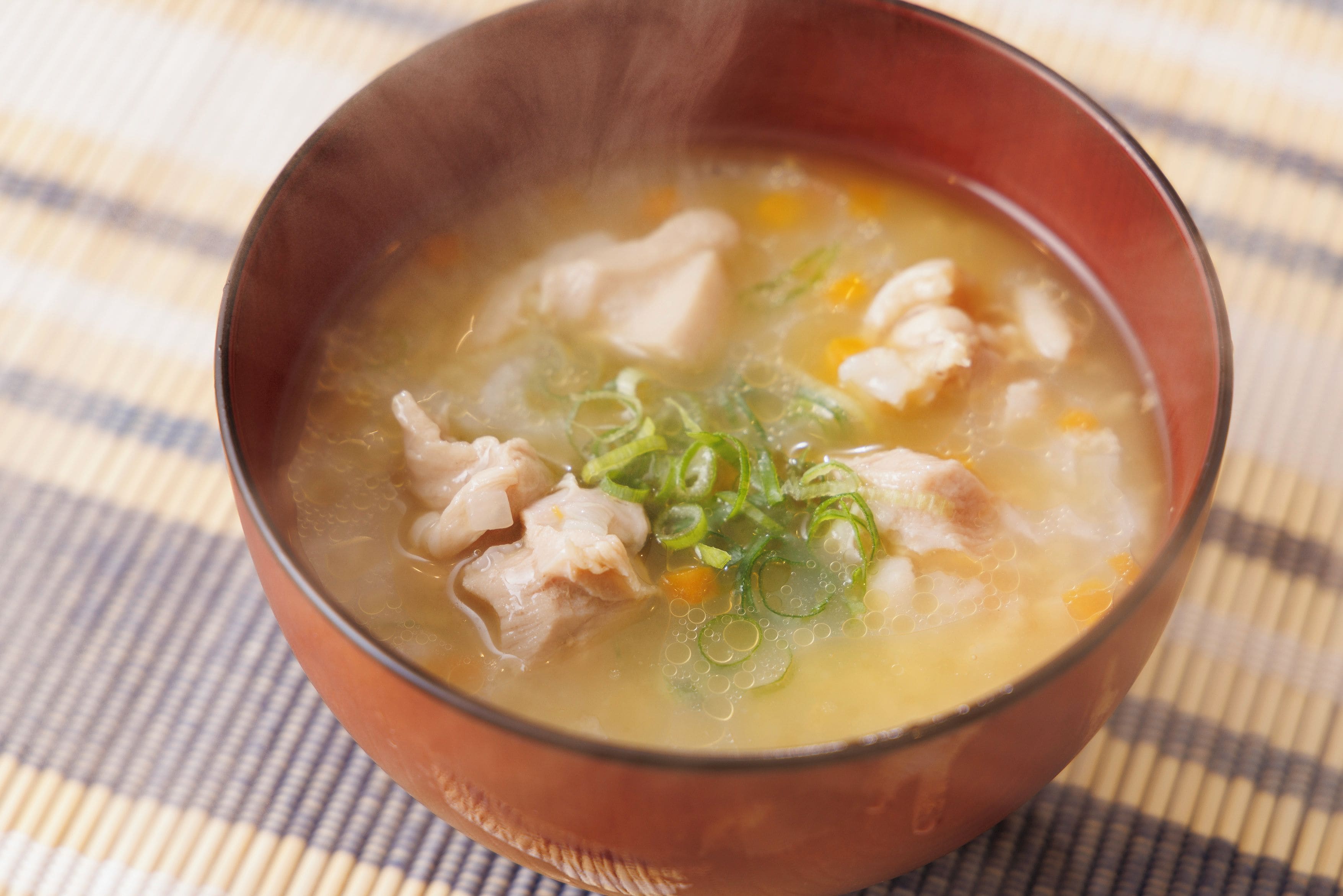 Un bol de sopa amb ingredients visibles com pollastre i verdures, servit en un bol de ceràmica sobre una sovina escamotada.