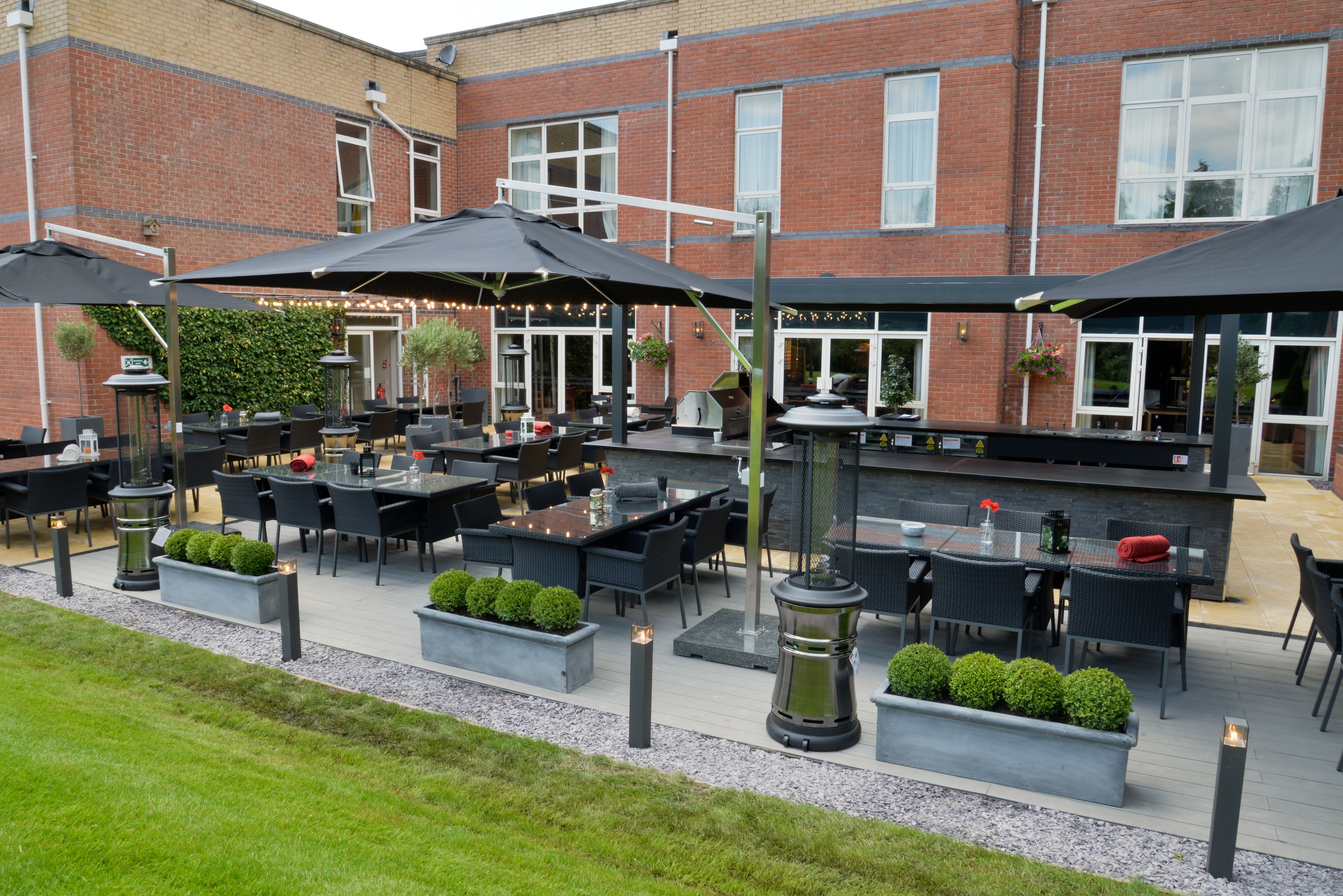 An outdoor patio area with tables and chairs, a barbecue grill, and potted plants.