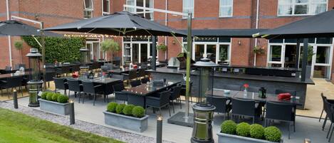 An outdoor patio area with tables and chairs, a barbecue grill, and potted plants.