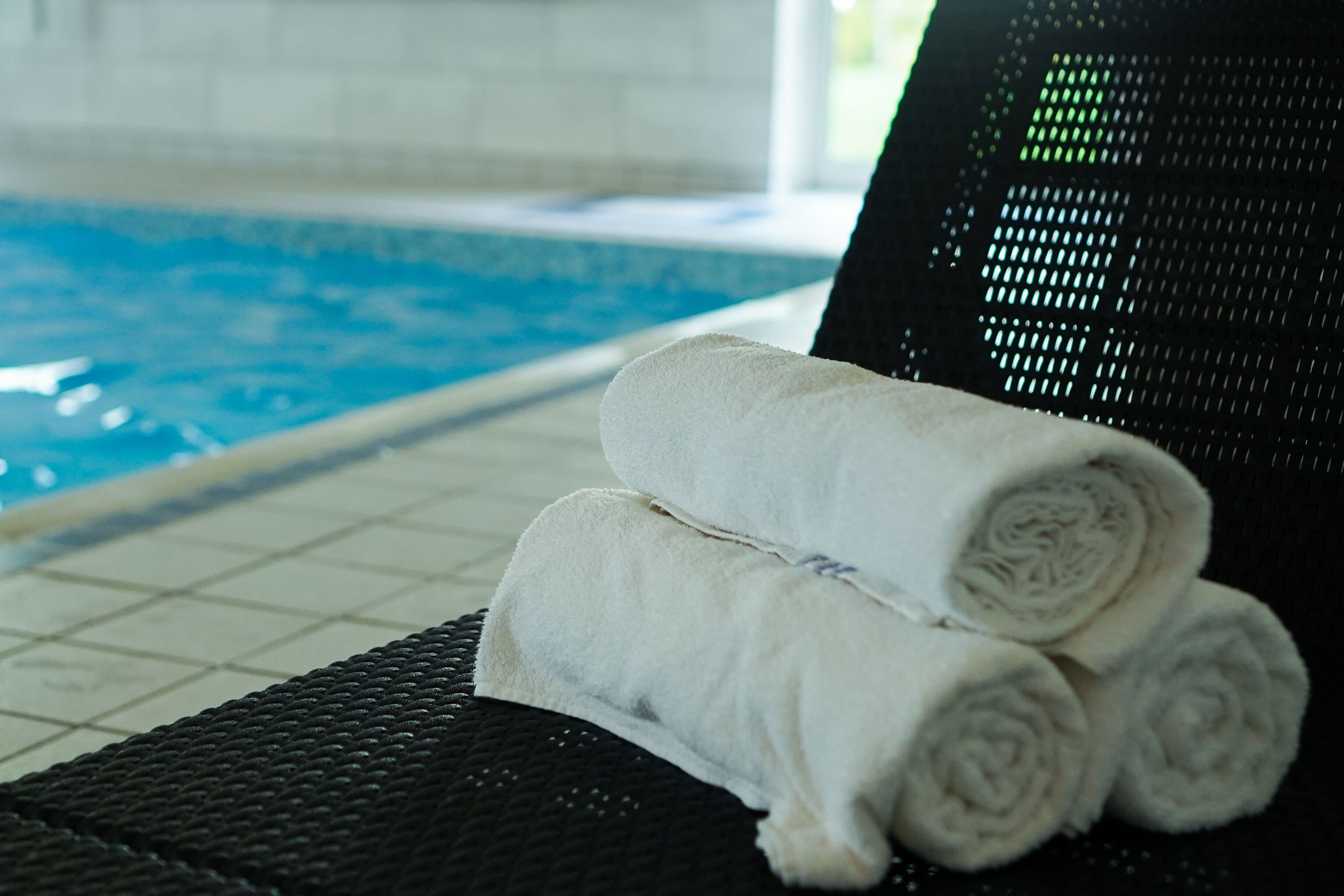 A poolside area with a black lounge chair and two rolled white towels.