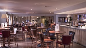 A spacious restaurant with multiple seating areas, including round tables and bar stools.