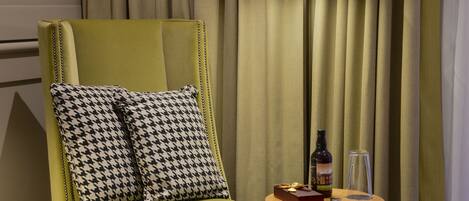 A green armchair with houndstooth pillows, a small round table with a bottle, glasses, and a box.