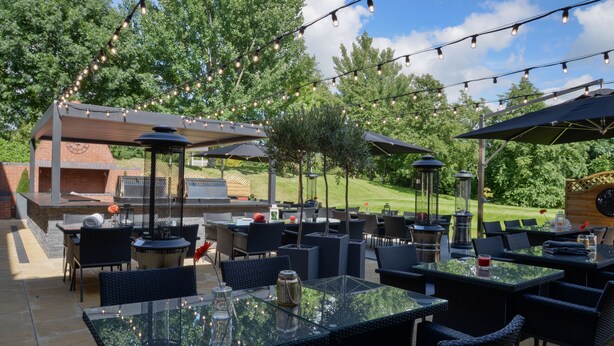 An outdoor patio area with tables and chairs, string lights, and a barbecue grill.