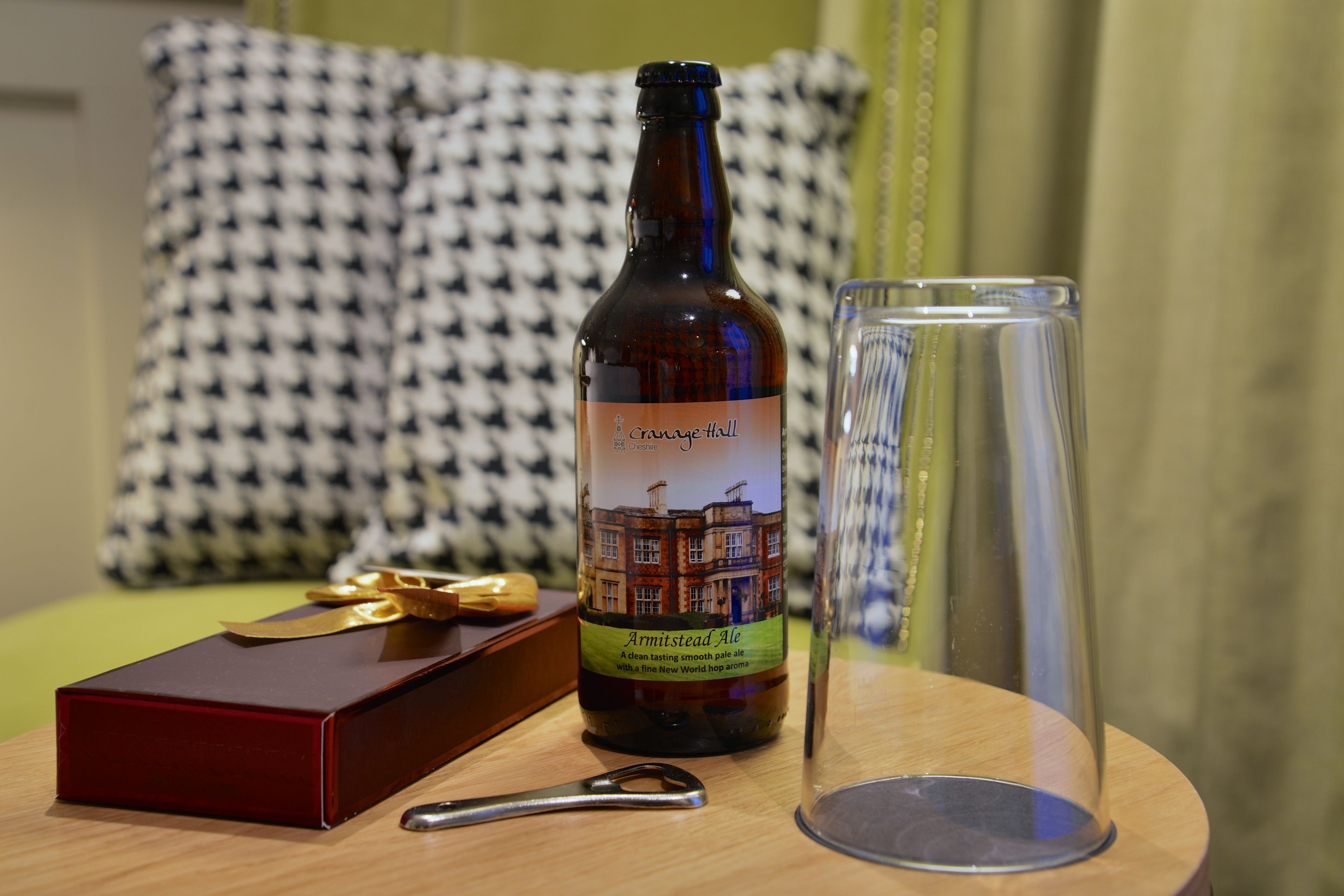 A bottle of Armitstead Ale, a pair of scissors, and an empty glass on a wooden table.
