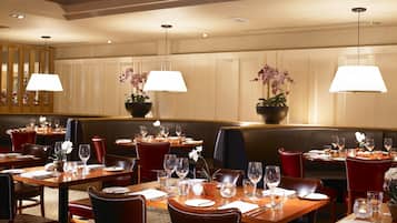 A restaurant with multiple tables set for dining, each with a lamp, wine glasses, and a flower centerpiece.