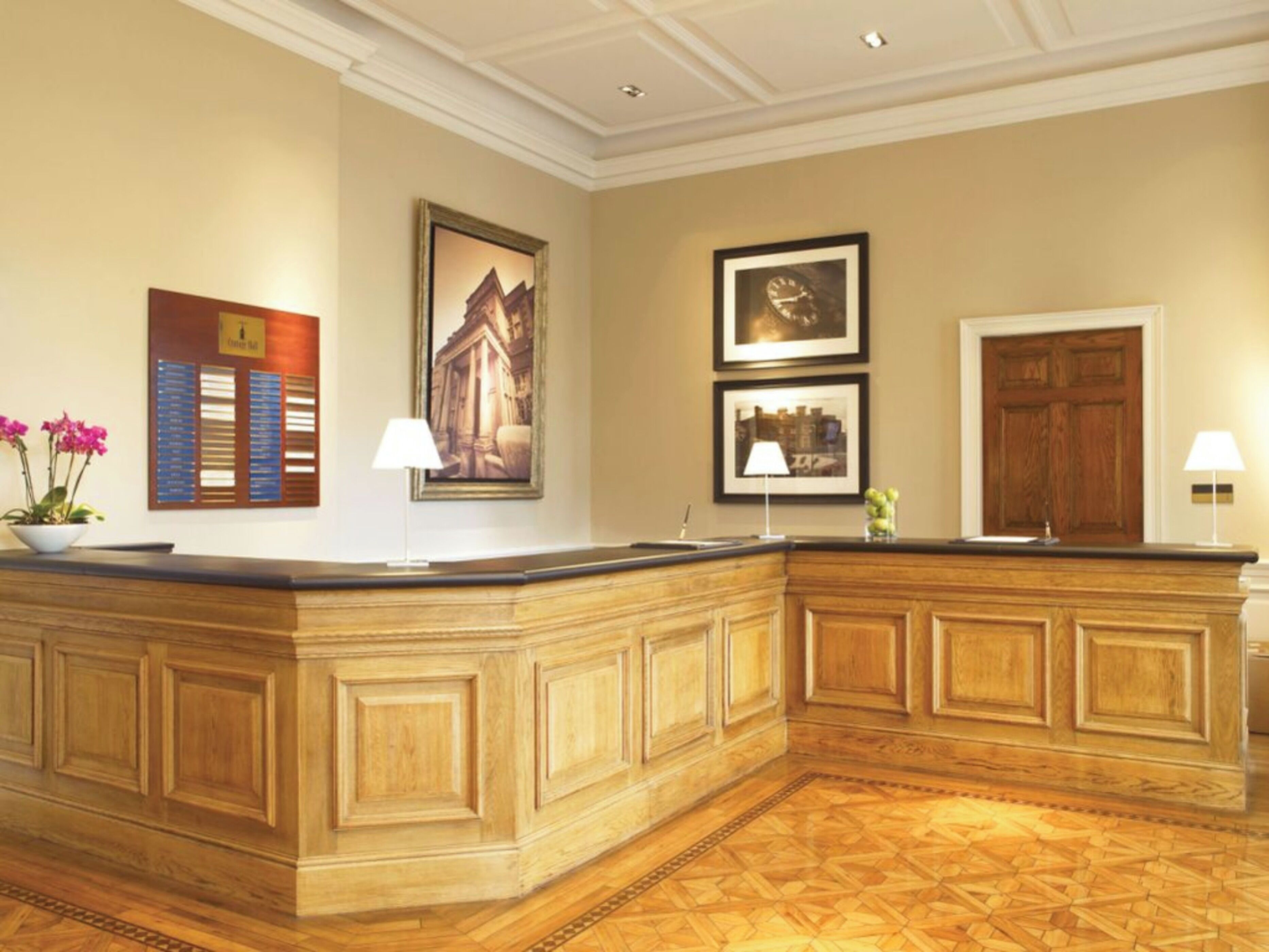 A reception area with a wooden reception desk, framed pictures on the wall, and a potted plant.