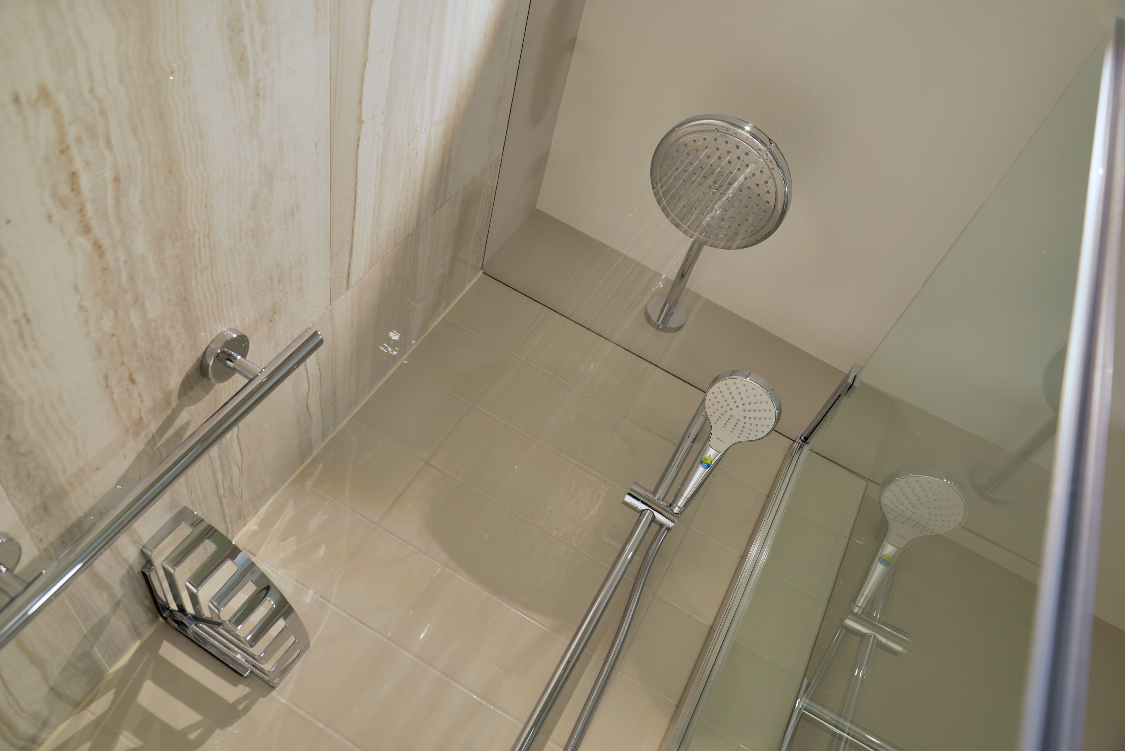 A glass-enclosed shower area with a handheld showerhead, a handheld showerhead with a circular head, and a shower caddy.